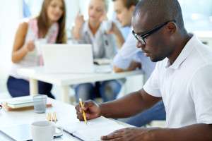 Portrait of young African guy looking in notepad in working environment